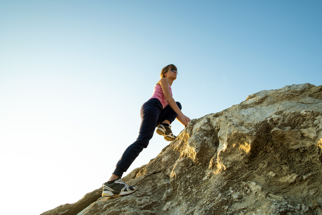 Woman hiker climbing steep big rock on a sunny day. Young fe